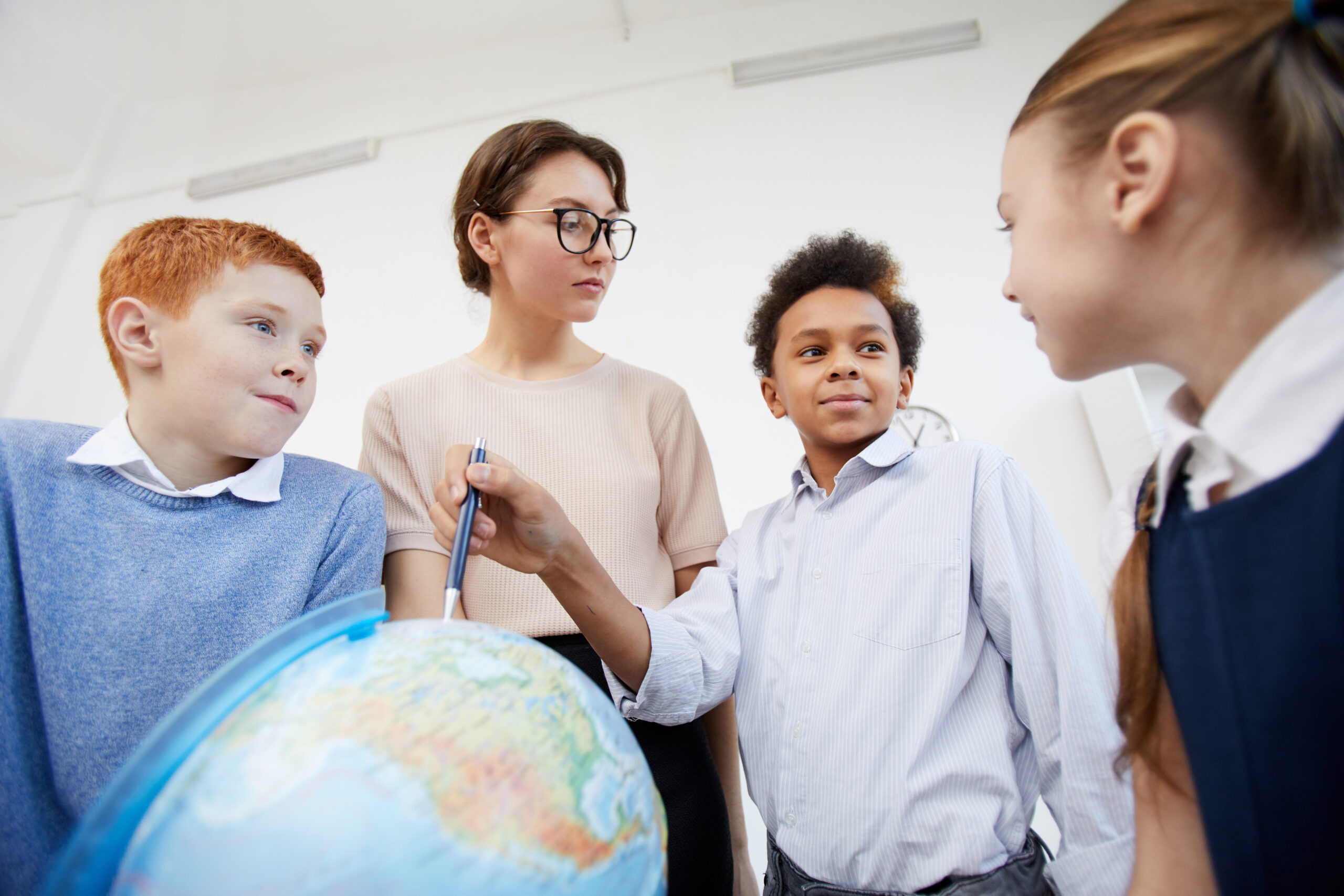 African schoolboy pointing at globe and telling about countries to his classmates and teacher during the lesson at school